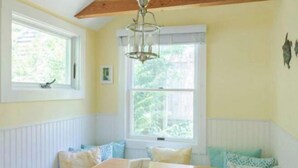 Una habitación acogedora con una mesa de madera, un banco blanco y una ventana con vistas a la vegetación.