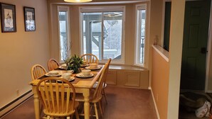 A dining area with a long wooden table, chairs, and a window with a view of a snowy landscape. - Schweitzer Mountain Condo (Sandpoint)