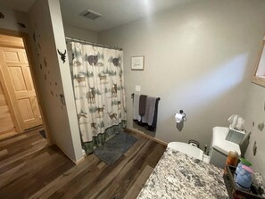 Een badkamer met een douchegordijn met hertenprint, een handdoekhouder met handdoeken, een toilet en een wastafel met spiegel.