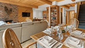 Una sala de estar acogedora con chimenea, un comedor listo para una comida, y una escalera que lleva a un nivel superior.