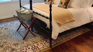 Un dormitorio con cama con dosel, una mesita de noche con cesta, un tapete estampado y vistas a la vegetación a través de la ventana.