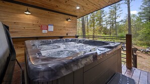 Una terrazza in legno con vasca idromassaggio, pareti in legno e vista sugli alberi.