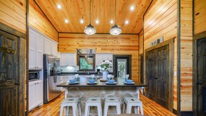 Una cucina con pareti in legno, un'isola centrale con sgabelli, mobili bianchi e un cartello con scritto 'KITCHEN'.