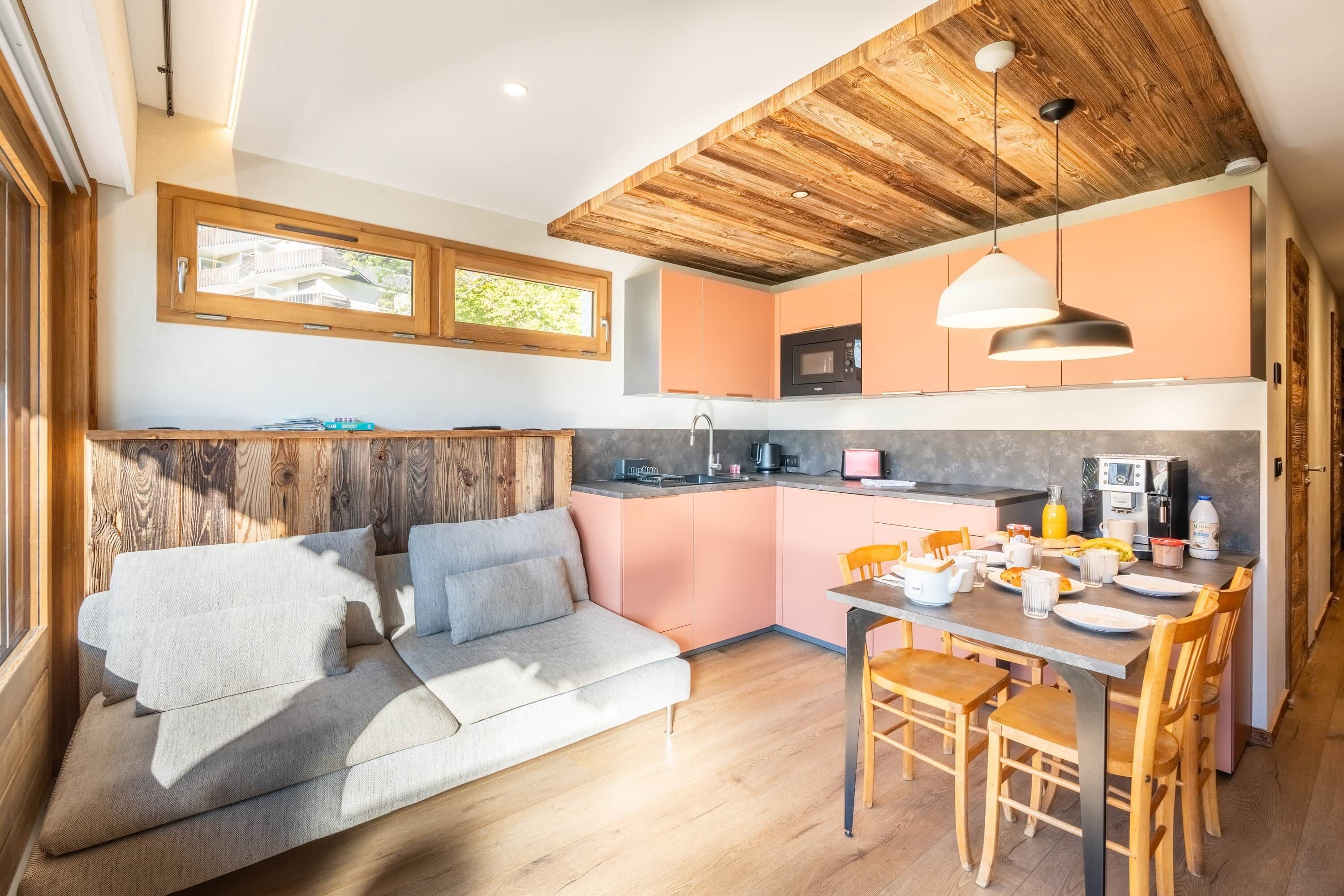 A modern kitchen with wooden ceiling, pink cabinets, and a dining area with a table and chairs.