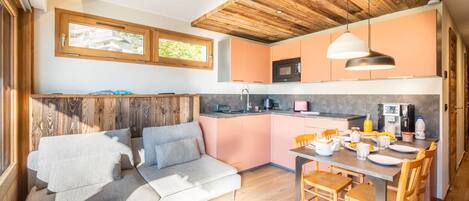 A modern kitchen with wooden ceiling, pink cabinets, and a dining area with a table and chairs.