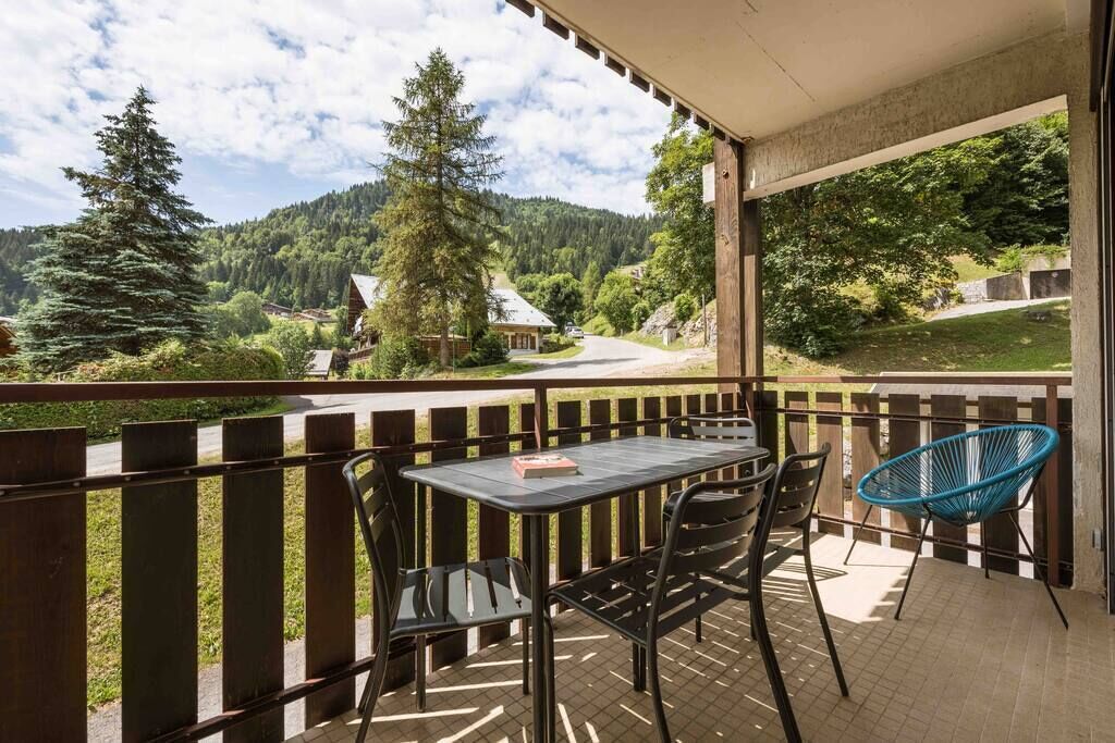 Un balcon avec une table et des chaises, donnant sur une vallée boisée.