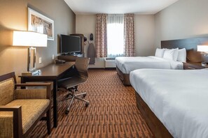 A hotel room with a desk, two beds, a television, and a window with curtains. - Suburban Studios Midland I-20 (Midland)