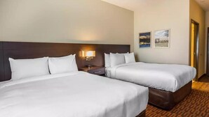A hotel room with two beds, a nightstand, a lamp, and two framed pictures on the wall. - Suburban Studios Midland I-20 (Midland)