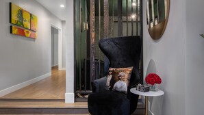 Un interior moderno con un sillón negro, un espejo redondo y una pequeña mesa con un florero de flores rojas.