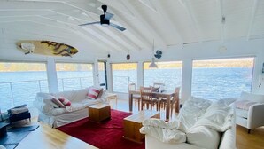 A spacious interior with a white sofa, a dining table, and chairs, a red rug, and a ceiling fan. - Lake Rosseau Sunset Facing Deep Water Lake Front Property (Port Carling)