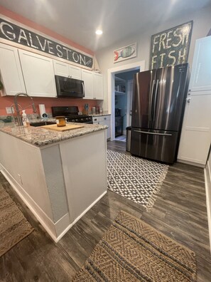 A modern kitchen with white cabinets, a stainless steel refrigerator, and a granite countertop.