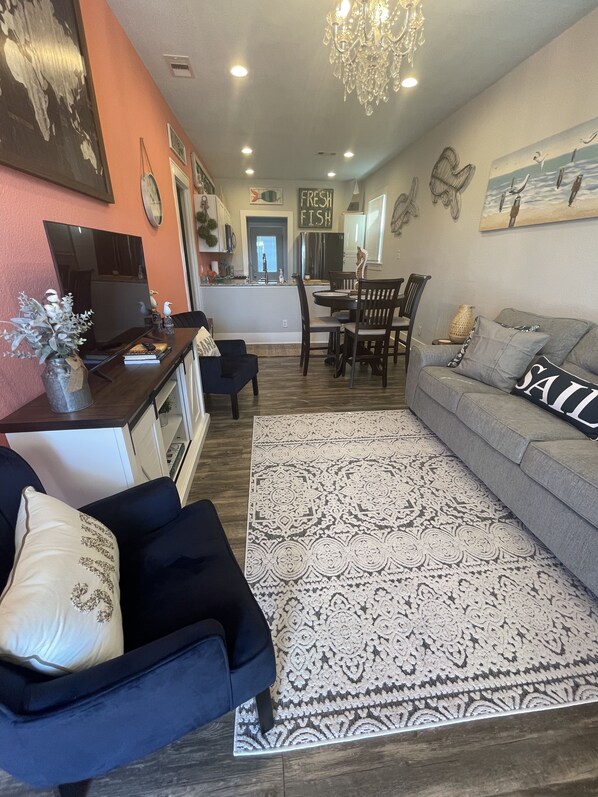 A living room with a sofa, chairs, a coffee table, a TV, and a dining area with a table and chairs.