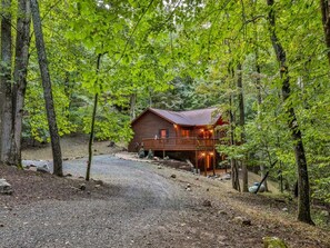 Une cabane entourée d’arbres, avec une allée de gravier menant à l’entrée.