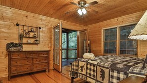 Un dormitori d'una cabana de fusta amb un llit, una petita taula de nit i un ventilador de sostre.