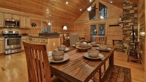 Interior d'una cabana de fusta amb taula de menjador per a quatre, electrodomèstics de cuina i una llar de pedra.
