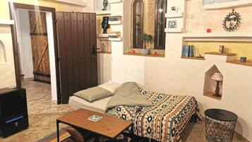 Una habitación pequeña y acogedora con una cama, una mesa de madera, un estante con libros, una lámpara y un adorno en la pared.