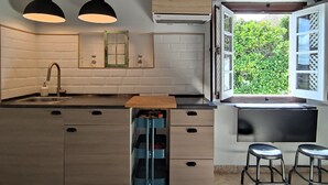 Une cuisine avec des poutres en bois, un évier, une fenêtre donnant sur un paysage verdoyant et deux tabourets de bar.
