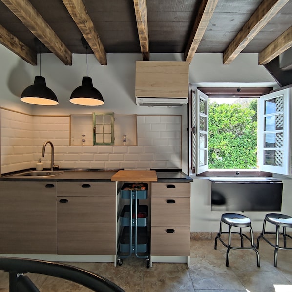 A kitchen with wooden beams, a sink, a window with a view of greenery, and two bar stools.