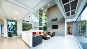 A spacious living area with a modern staircase, a flat-screen TV mounted on the wall, and a large window offering a view of greenery. - Luxury Villa Los Pajaros Private Pool & Oceanview (Playa Hermosa)