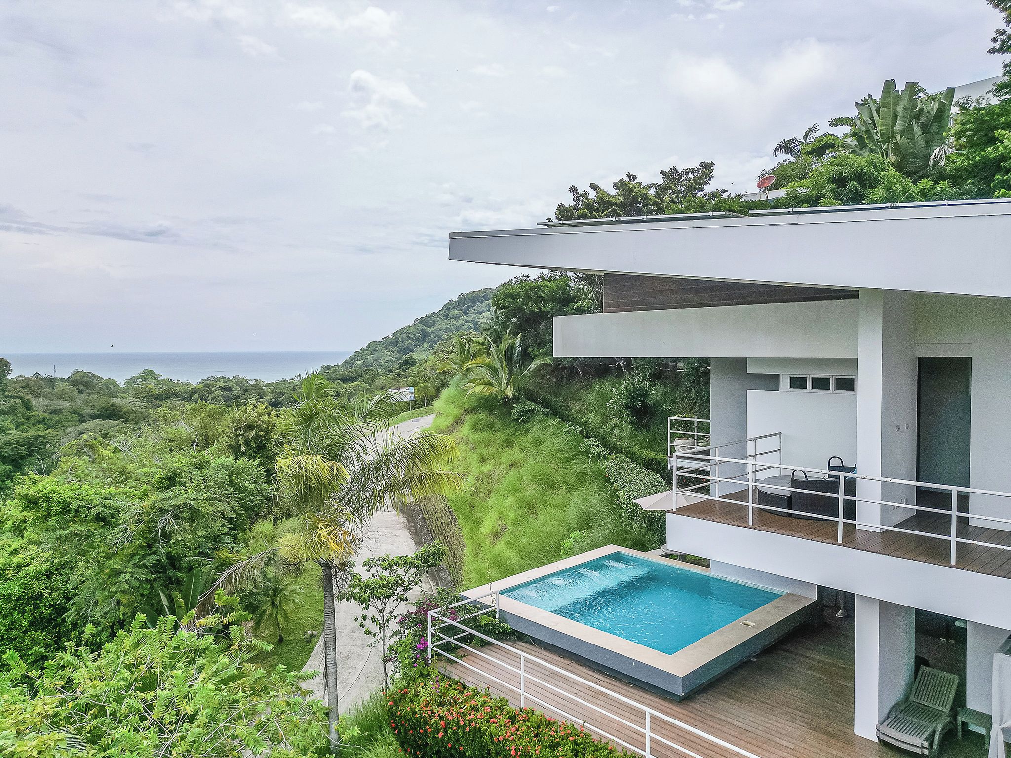 A modern house with a pool, surrounded by lush greenery and overlooking a body of water.