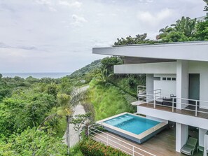 Une maison moderne avec piscine, entourée d’une végétation luxuriante et offrant une vue sur un plan d’eau.
