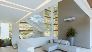 A modern interior with a staircase, a sectional sofa, and a large window with a view of greenery. - Luxury Villa Los Pajaros Private Pool & Oceanview (Playa Hermosa)