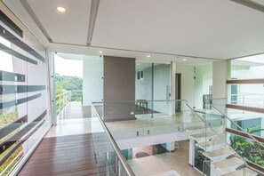 A modern interior with a glass balustrade, a staircase, and a view of greenery outside.