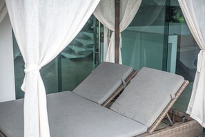 A room with a glass partition, a bed with grey bedding, and white curtains.