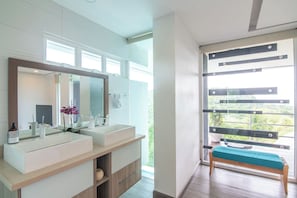 A modern bathroom with a large mirror, dual sinks, and a bench by a large window.