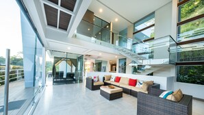 A spacious living area with a high ceiling, a glass staircase, and a view of greenery outside. - Luxury Villa Los Pajaros Private Pool & Oceanview (Playa Hermosa)