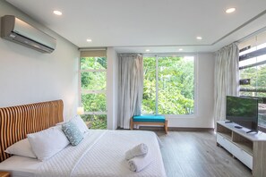 A hotel room with a bed, a TV, a window with curtains, and an air conditioning unit.