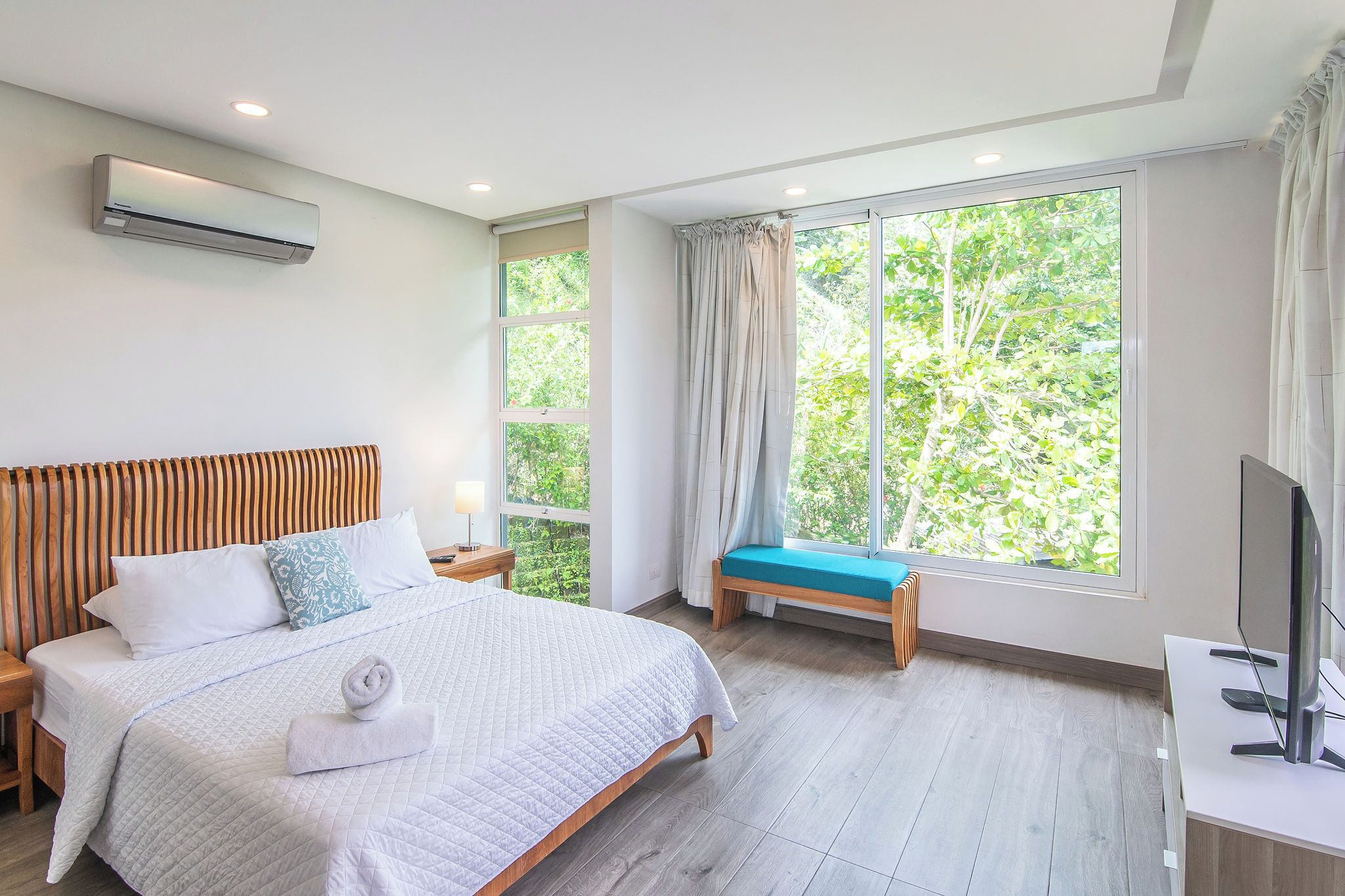 Une chambre d’hôtel équipée d’un lit, d’une table de chevet, d’une télévision, d’une fenêtre avec des rideaux et d’un appareil de climatisation.