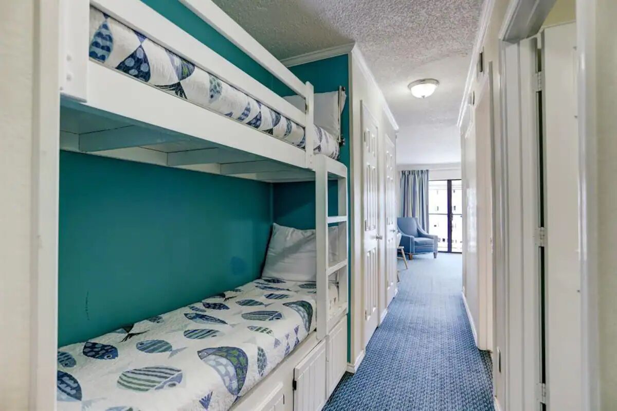 A bunk bed room with teal walls and a blue carpeted hallway.