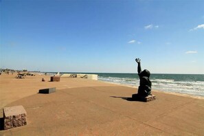 A beach with a statue of a person raising their hand, a clear sky, and the ocean in the background. - It's a Shore Thing (Galveston)