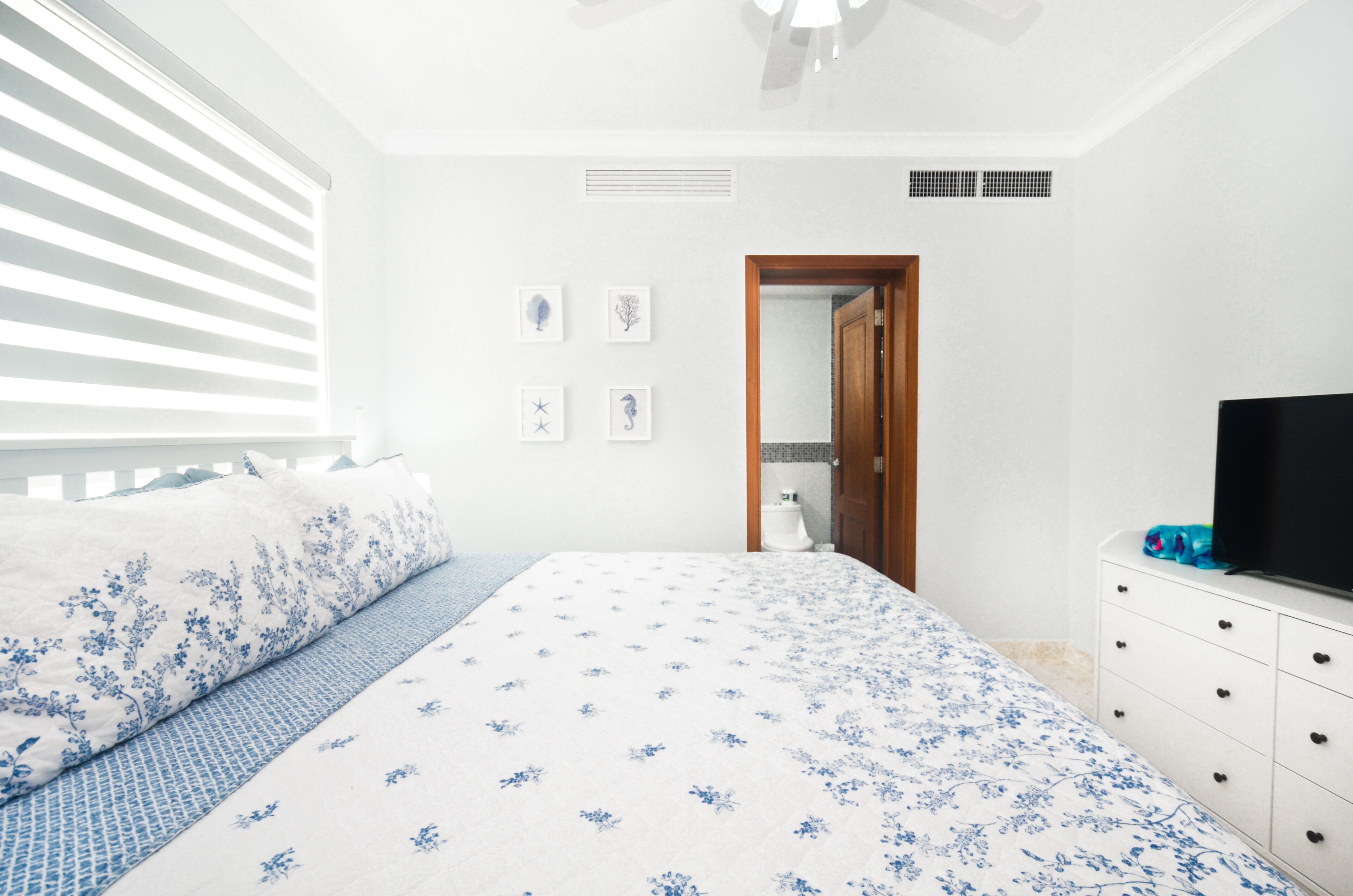 Quarto com cama, penteadeira, televisão e porta para o banheiro.
