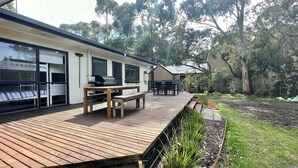 Ein modernes Haus mit einer Holzterrasse, einem Grillbereich und einem Garten.