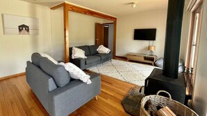 Ein modernes Wohnzimmer mit grauem Sofa, Holzboden, großem Spiegel, Kamin und Fernseher.