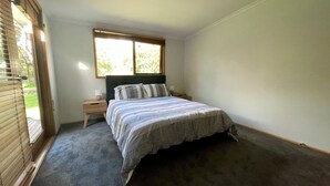Ein Schlafzimmer mit Bett, Nachttisch, Fenster und Tür.