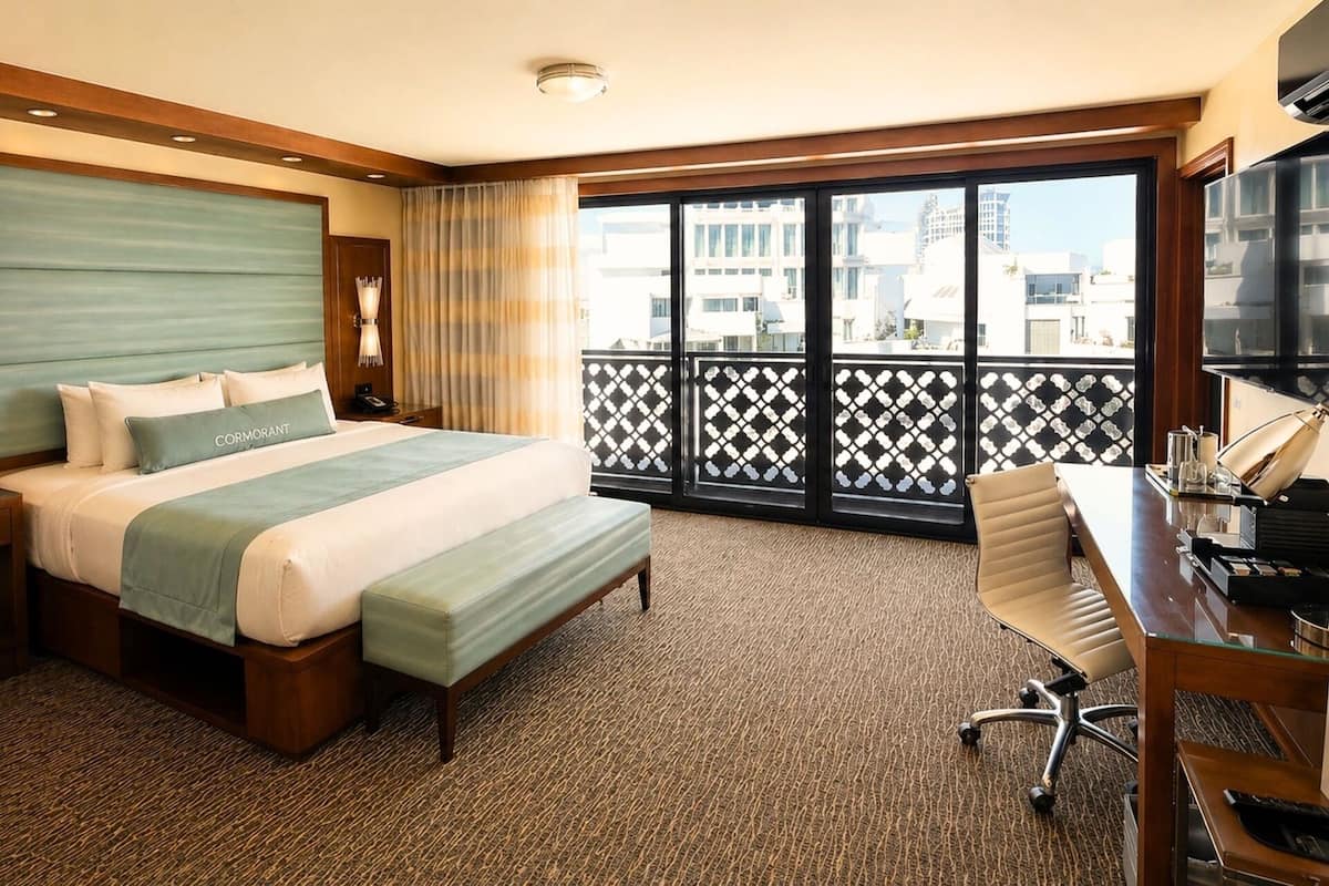Una habitación de hotel con cama, escritorio y ventanas amplias.