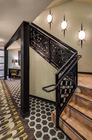 A staircase with a geometric patterned carpet, a black metal railing, and wall-mounted lights.