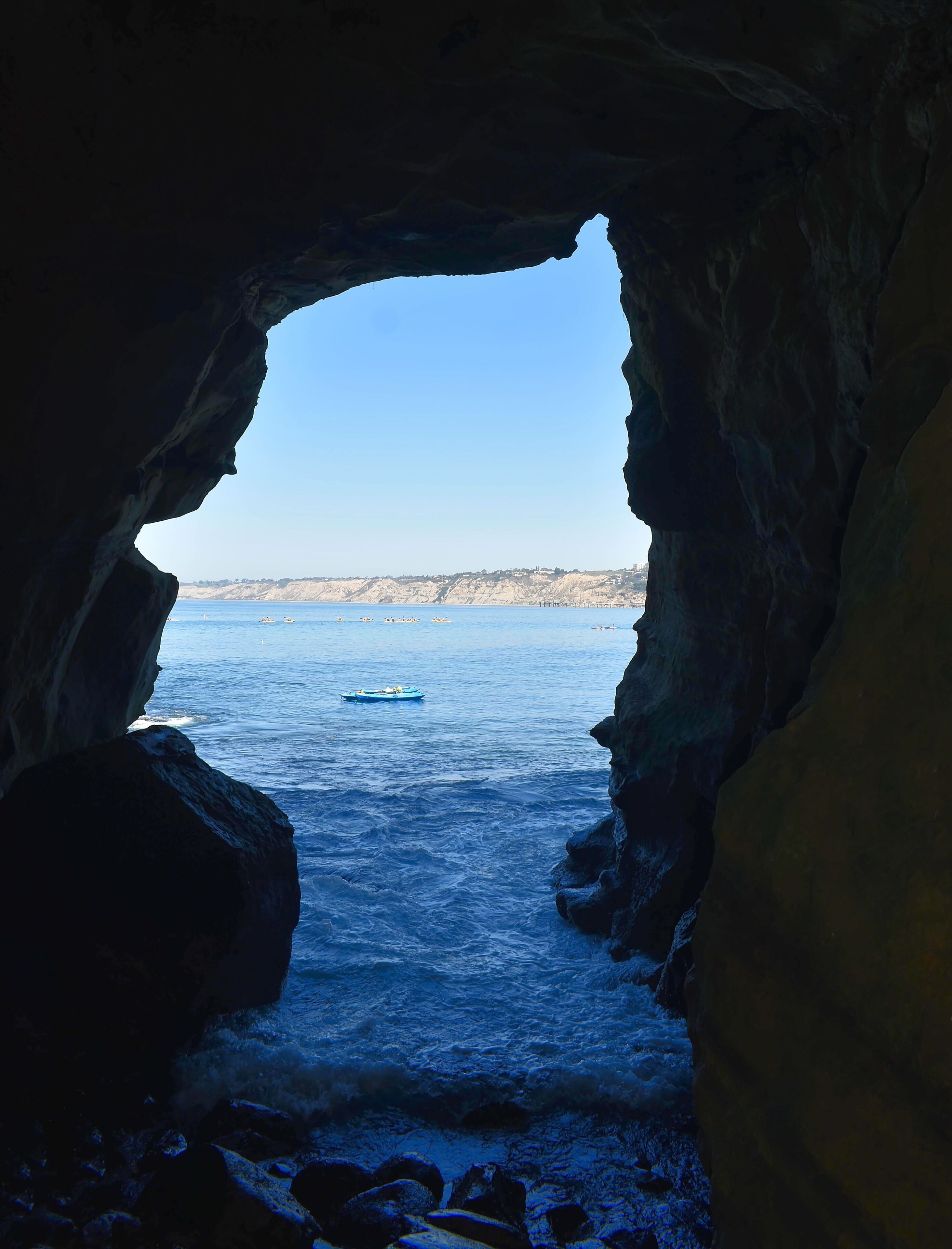 A view through a cave opening to a coastal area with boats on the water.