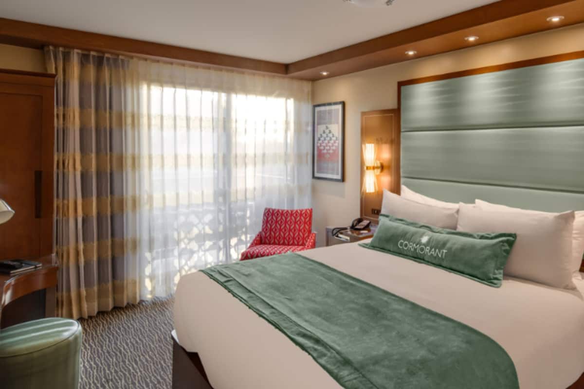 Una habitación de hotel con una cama grande, una mesita de noche, una lámpara y una ventana con cortinas.