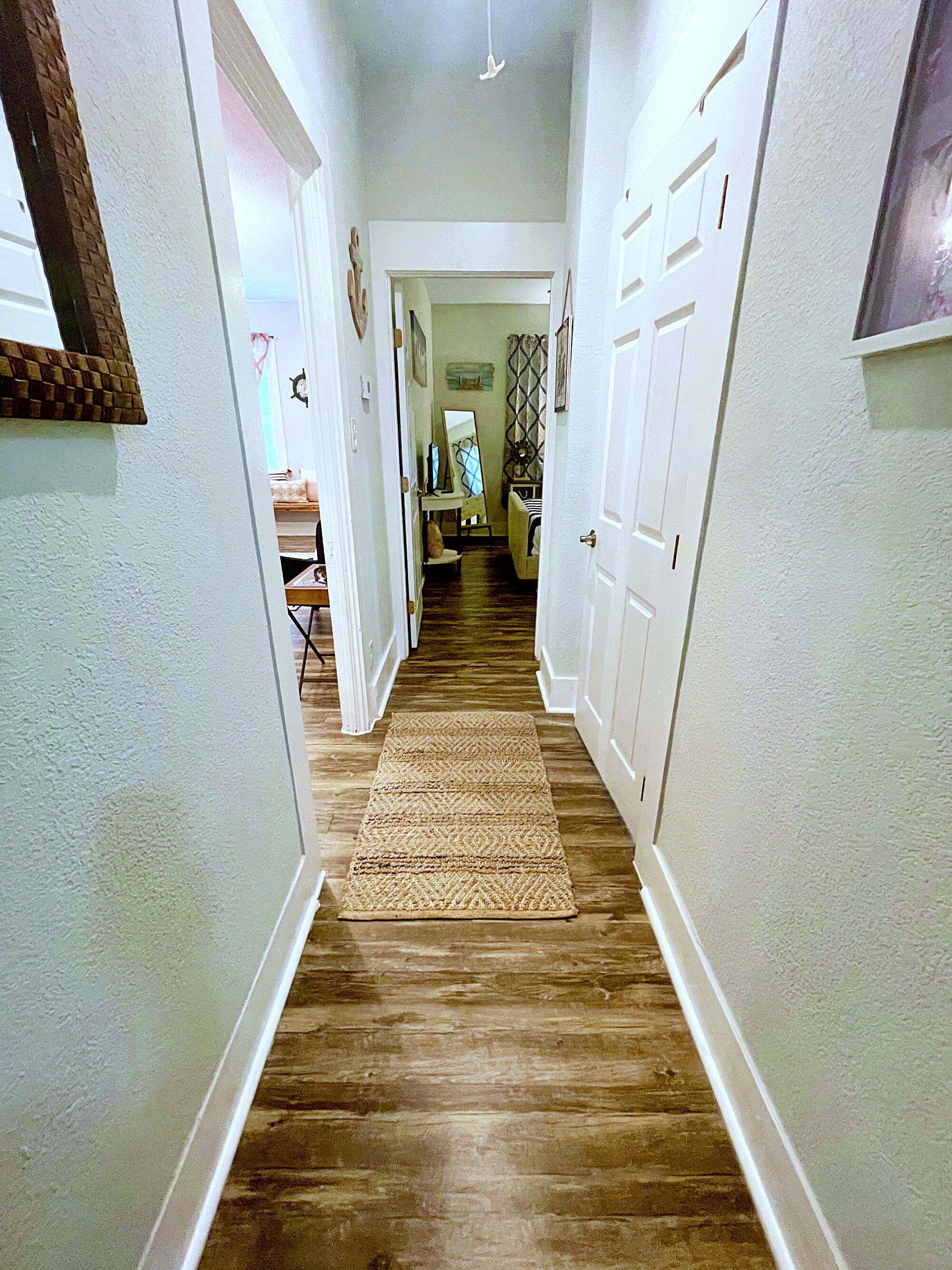 A hallway with wooden flooring, white walls, and a doormat at the entrance.