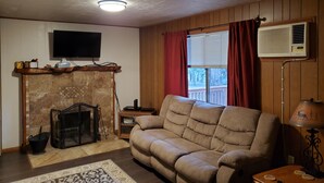 Ein Wohnzimmer mit Kamin, einer Couch, einem Fernseher und einem Fenster mit Vorhängen.