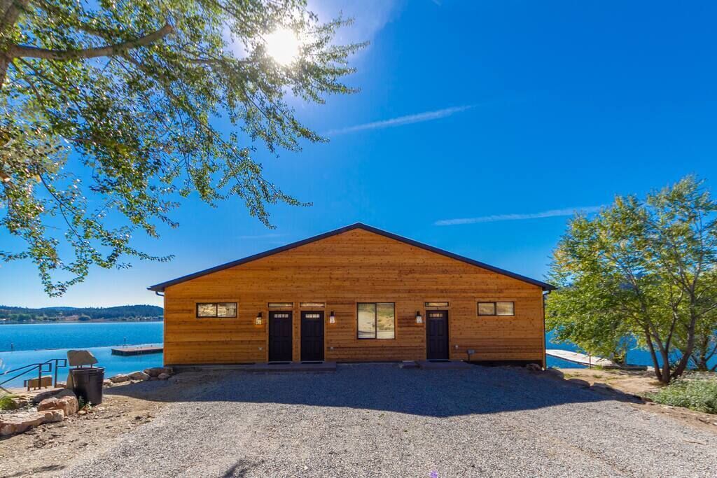 Una cabaña de madera con camino de grava, un muelle y vista a un lago.