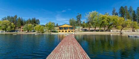 A wooden pier leading to a yellow building with large windows, surrounded by trees and water.