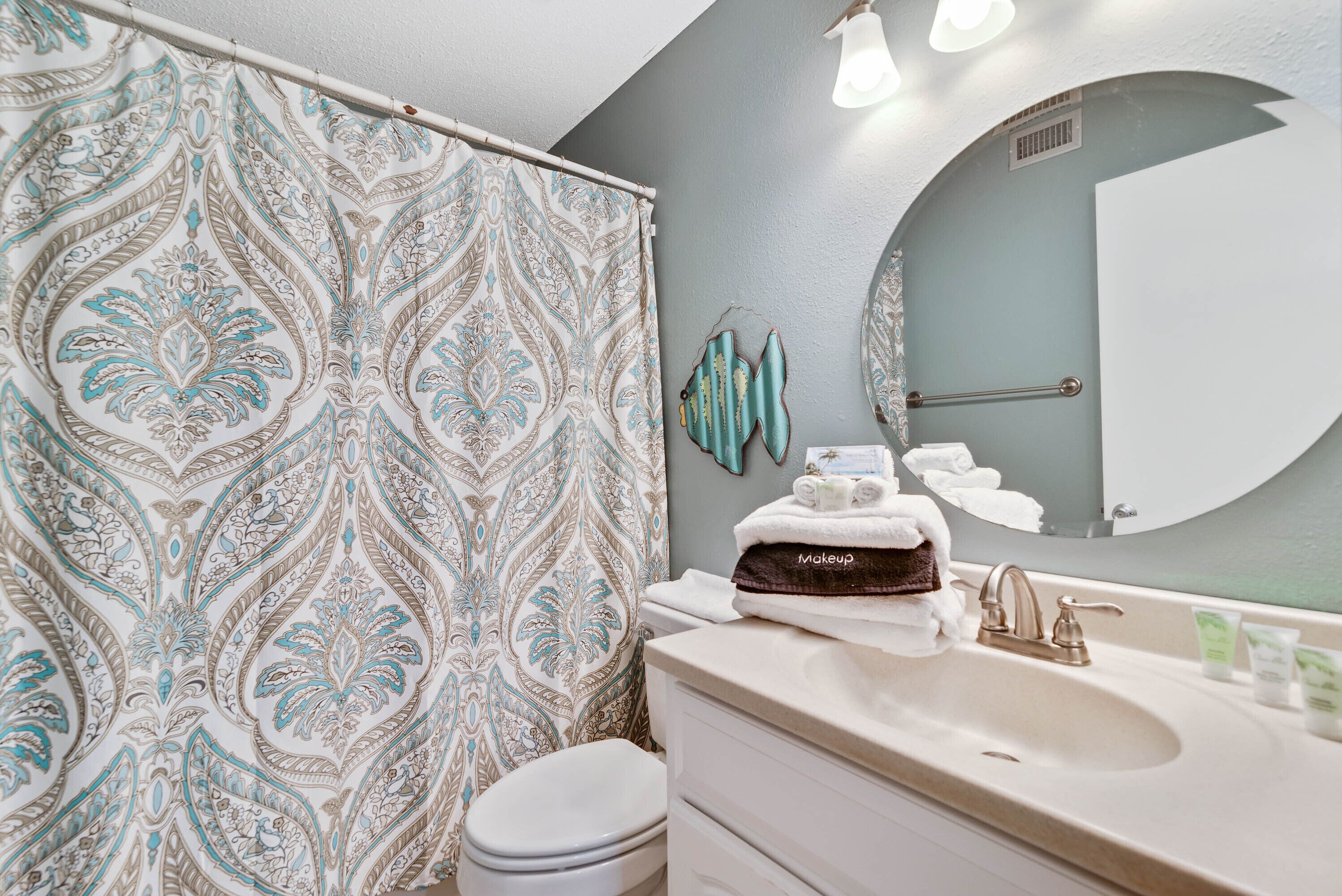 A bathroom with a patterned shower curtain, a white toilet, a sink with toiletries, and a mirror.