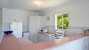Une cuisine équipée d’un réfrigérateur, d’un four à micro-ondes, d’une cuisinière et d’une fenêtre donnant sur la forêt.