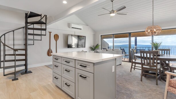 A modern kitchen with a central island, a spiral staircase, and a dining area with a view. - Ma'alaea Surf, D9 - Oceanfront Condo - remodeled two-bedroom, 2nd Floor (Kihei)