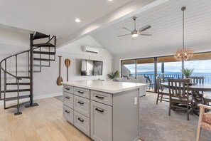 A modern kitchen with a central island, a spiral staircase, and a dining area with a view. - Ma'alaea Surf, D9 - Oceanfront Condo - remodeled two-bedroom, 2nd Floor (Kihei)